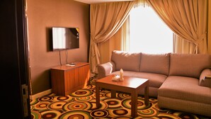 A hotel room with a sofa, a small table, a TV on the wall, and a window with curtains. - Beyab Al Azizeyyah Hotel (Makkah)