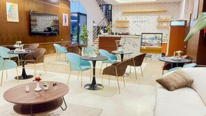 A modern hotel lobby with a mix of seating options including round tables and sofas, a reception desk, and a staircase leading to upper floors. - Beyab Al Azizeyyah Hotel (Makkah)