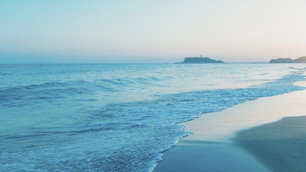 Una playa con mar tranquilo, una orilla arenosa y una isla distante con un faro.