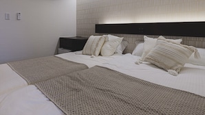 Una cama bien hecha con una manta estampada, un cabecero con un panel de color claro y una mesita de noche con un control remoto.