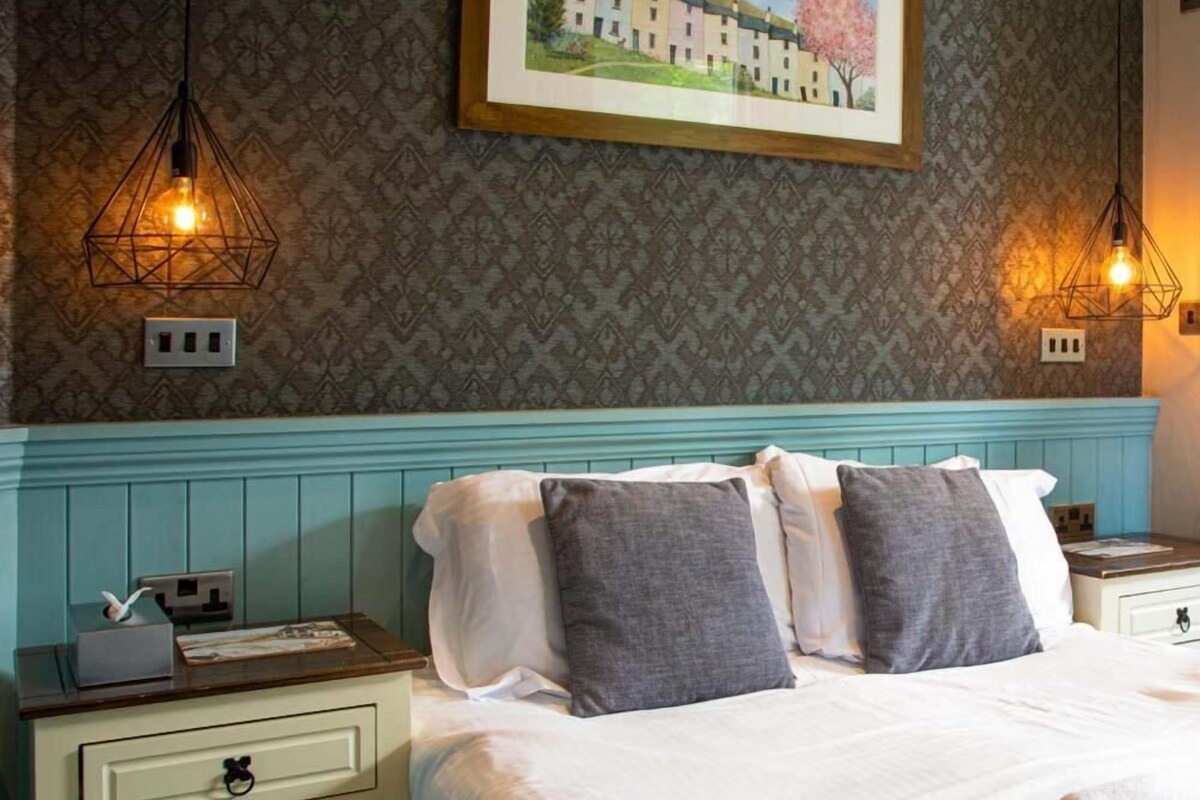 A neatly made bed with pillows, a nightstand with a lamp, and a wall with a framed picture.