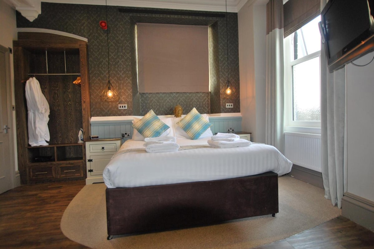 A hotel room with a large bed, a wardrobe, a mirror, and a window.