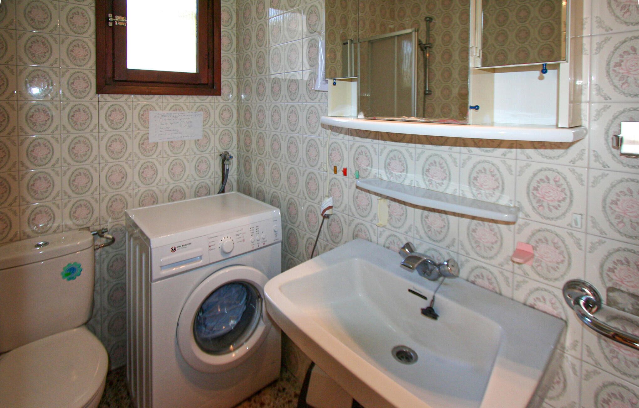 Un baño con lavadora, inodoro, lavamanos y un espejo sobre el lavamanos.
