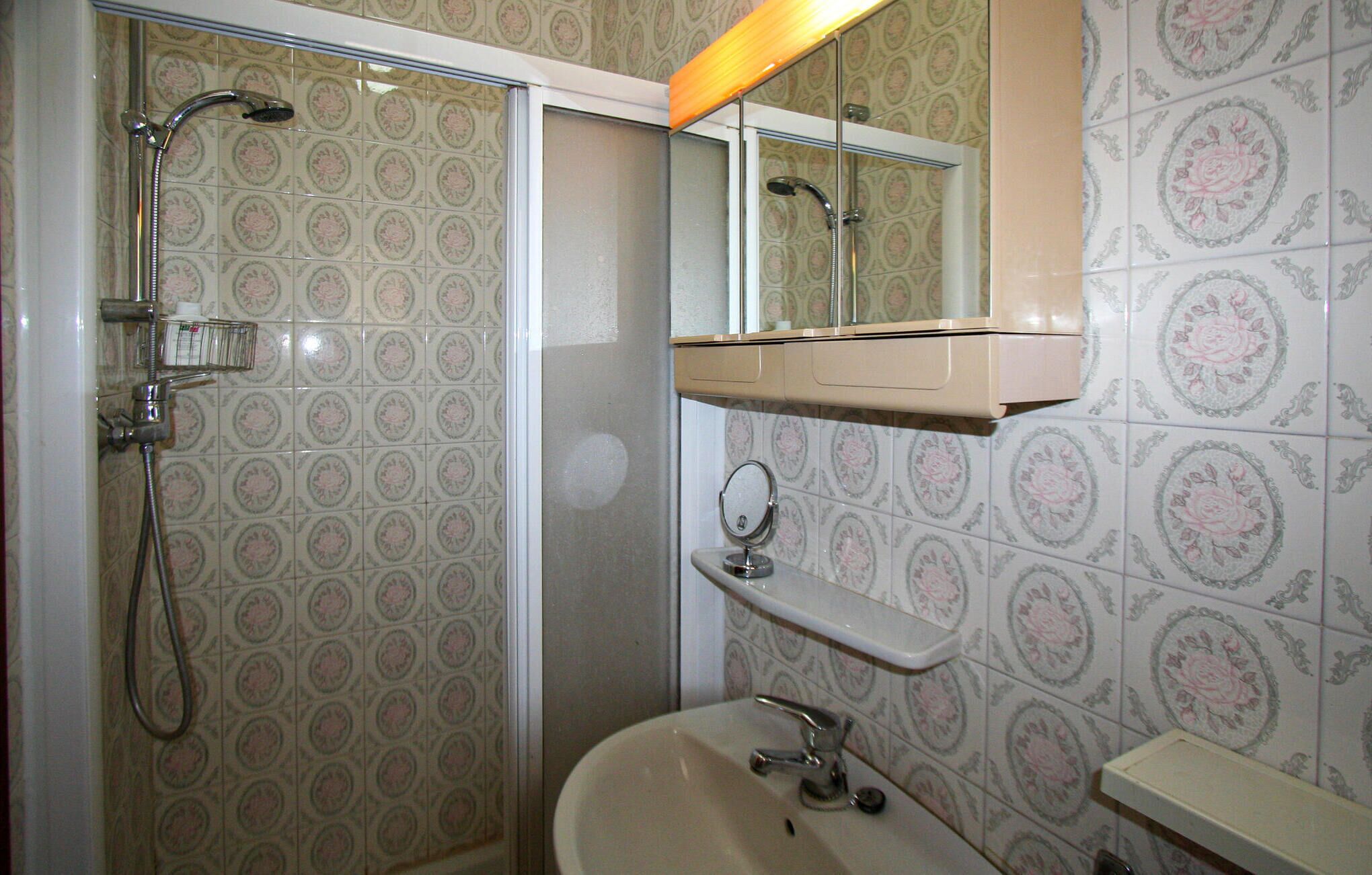 Une salle de bain équipée d’une douche, d’un lavabo, d’un miroir et d’un meuble-lavabo avec une étagère.