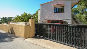 A two-story house with a white exterior and a red roof, a gated entrance, and a staircase leading to a red car parked inside.