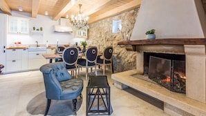 A cozy living area with a stone fireplace, wooden ceiling beams, and a dining set. - Villa Jelena (Novi Vinodolski)