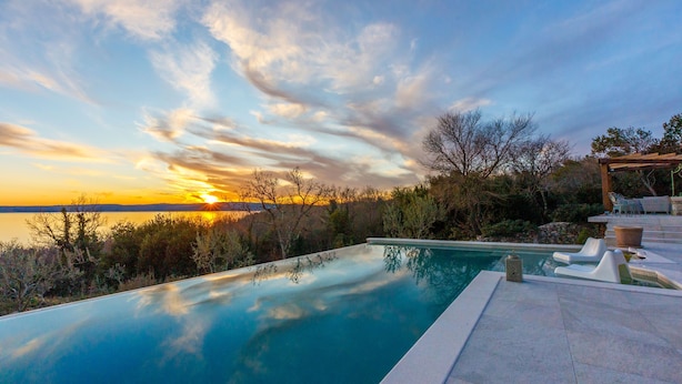 A swimming pool with a view of the sunset over a body of water, surrounded by trees and a pergola. - Villa Jelena (Novi Vinodolski)