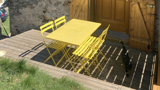 A rustic wooden building with a stone exterior, a wooden door, and a yellow table and chairs outside. - BRIGHT, SPACIOUS, COSY BARN AT THE FOOT OF THE CHEMIN DE SAINT-JACQUES (GAVARNIE GEDRE)