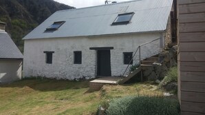 A white building with a metal roof, a small porch, and a staircase leading to a door. - BRIGHT, SPACIOUS, COSY BARN AT THE FOOT OF THE CHEMIN DE SAINT-JACQUES (GAVARNIE GEDRE)