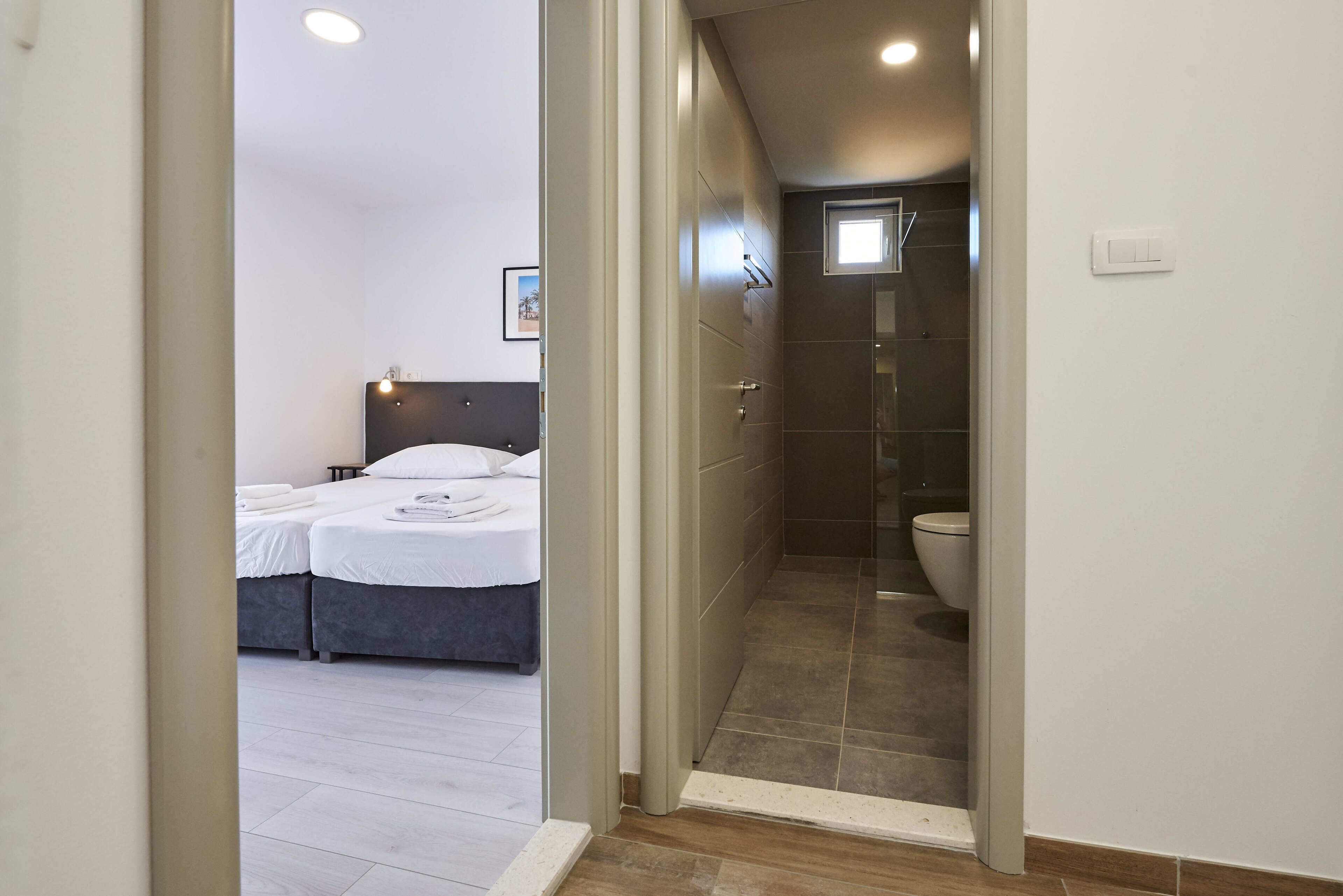 Una habitación de hotel moderna con cama, mesitas de noche y un baño con ducha e inodoro.