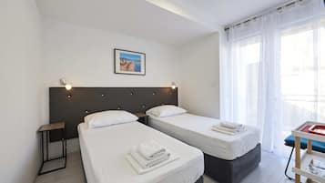 Habitación de hotel con dos camas, una mesita de noche, un cuadro enmarcado en la pared y una ventana con cortinas traslúcidas.