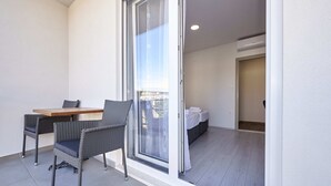 Un balcón con mesa y sillas, un ventanal corredero que da a un dormitorio y un ventilador de techo.