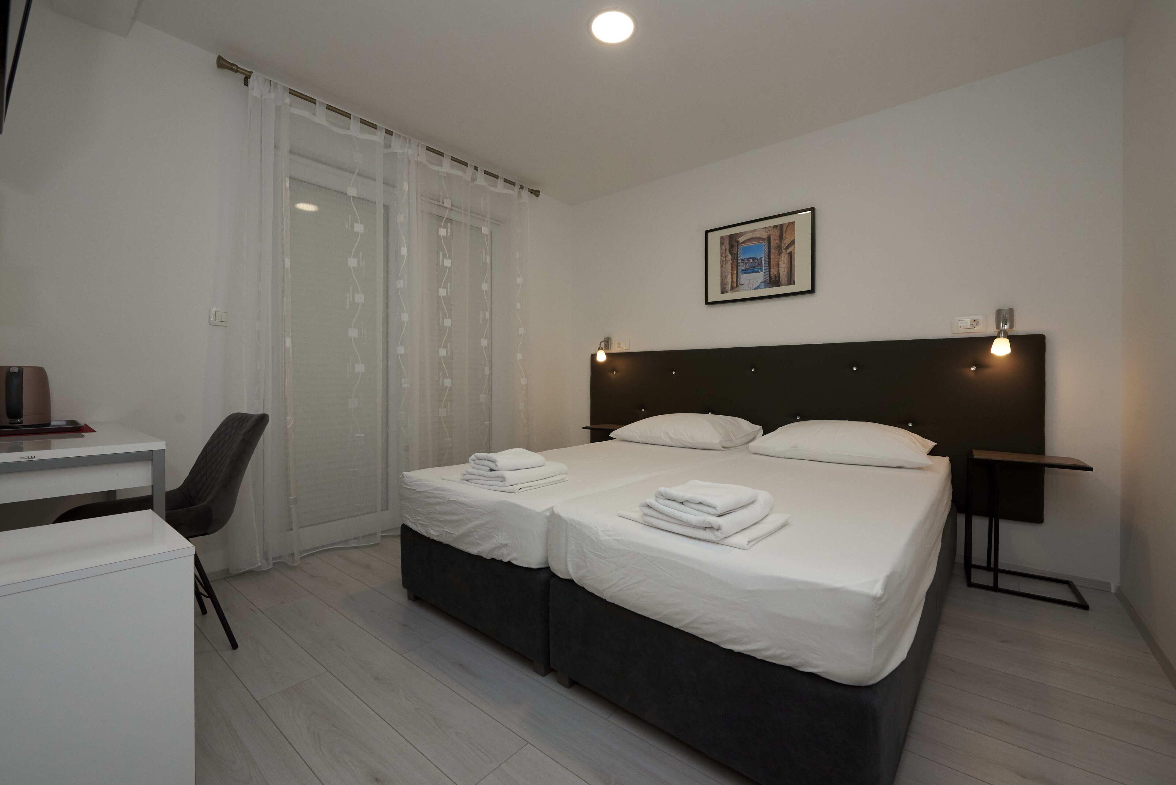 A hotel room with two beds, a desk, a chair, and a nightstand.