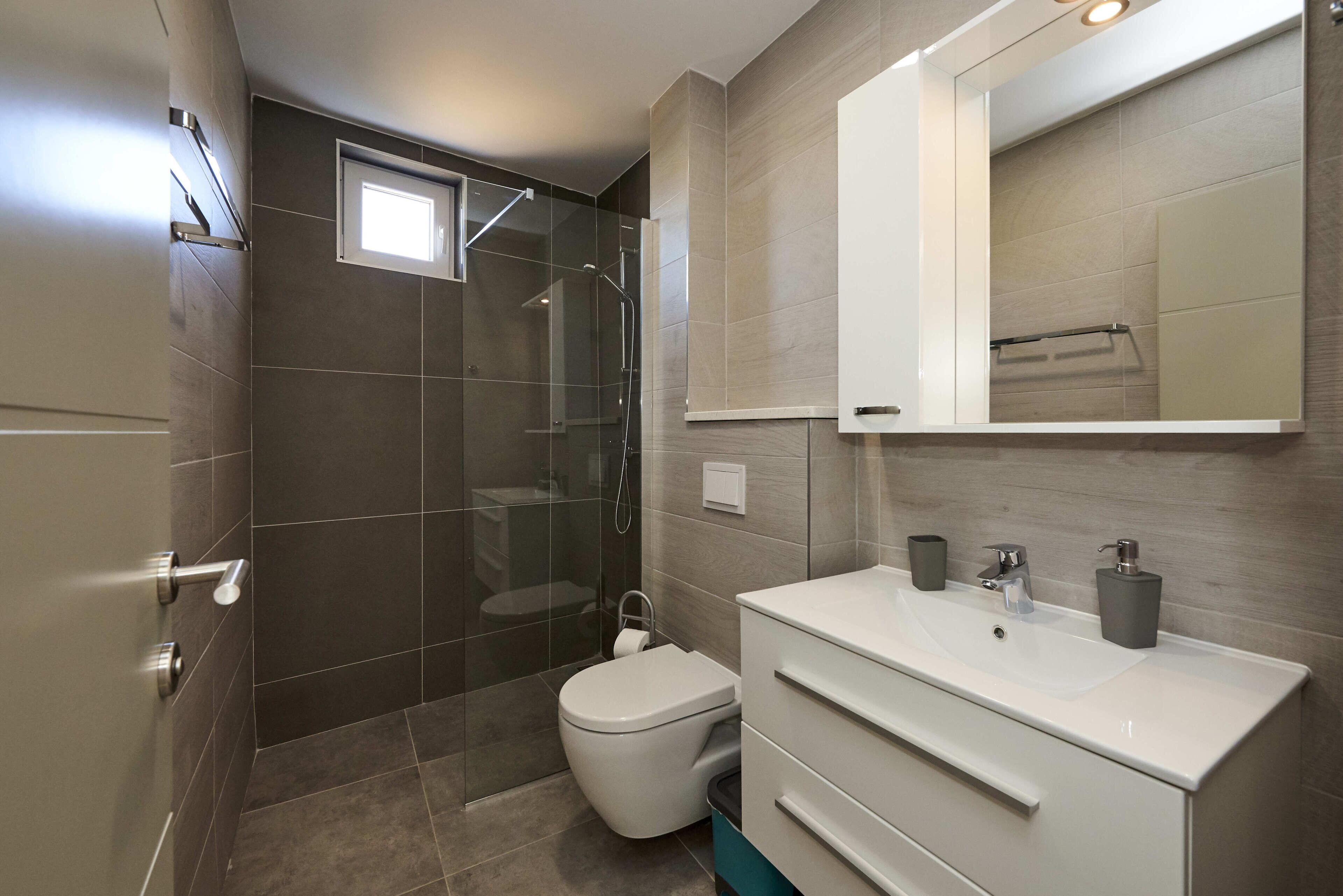 Un baño moderno con ducha de vidrio, inodoro y tocador con espejo y lavamanos.