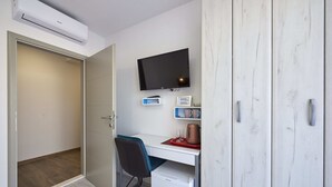 Una habitación compacta con escritorio, televisión, refrigerador pequeño y armario.