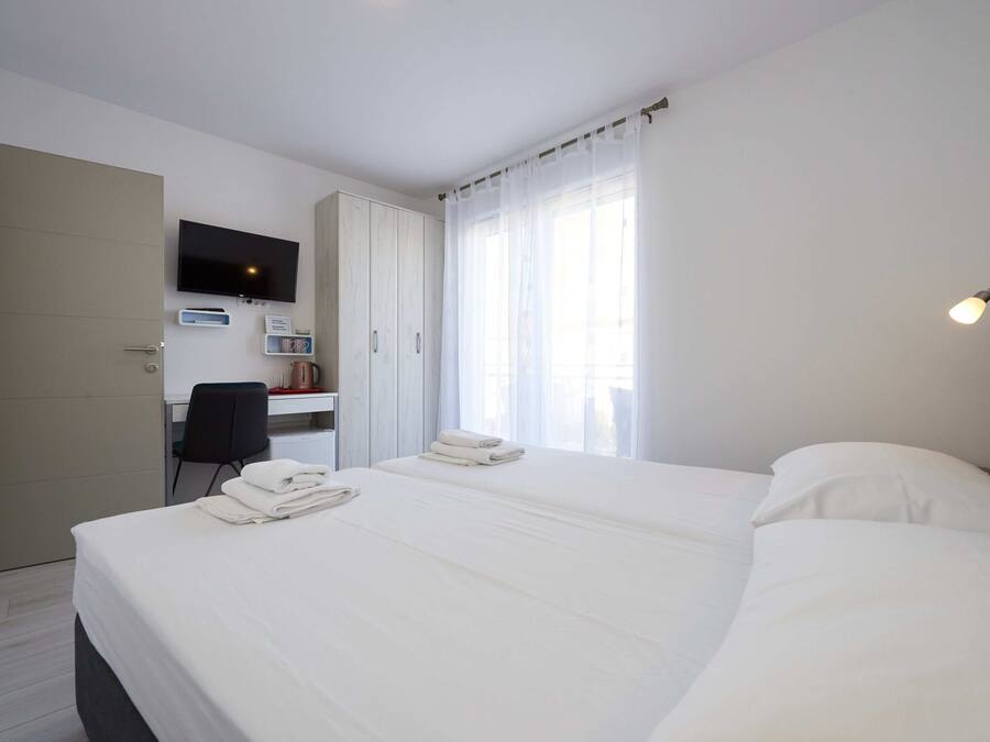 A hotel room with a bed, a desk with a chair, a television, and a window with curtains.