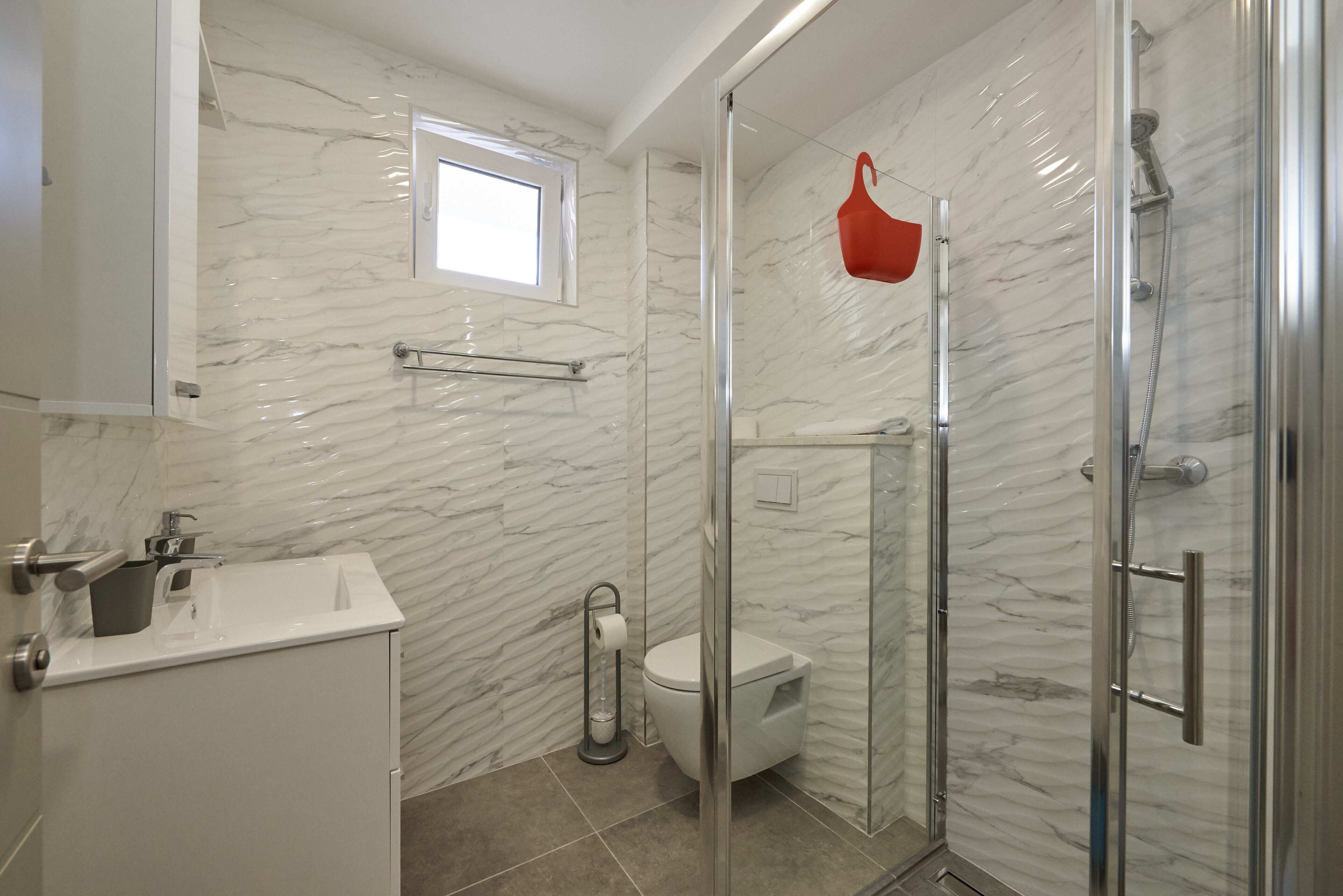 Un baño moderno con ducha de vidrio, lavamanos blanco y un inodoro.
