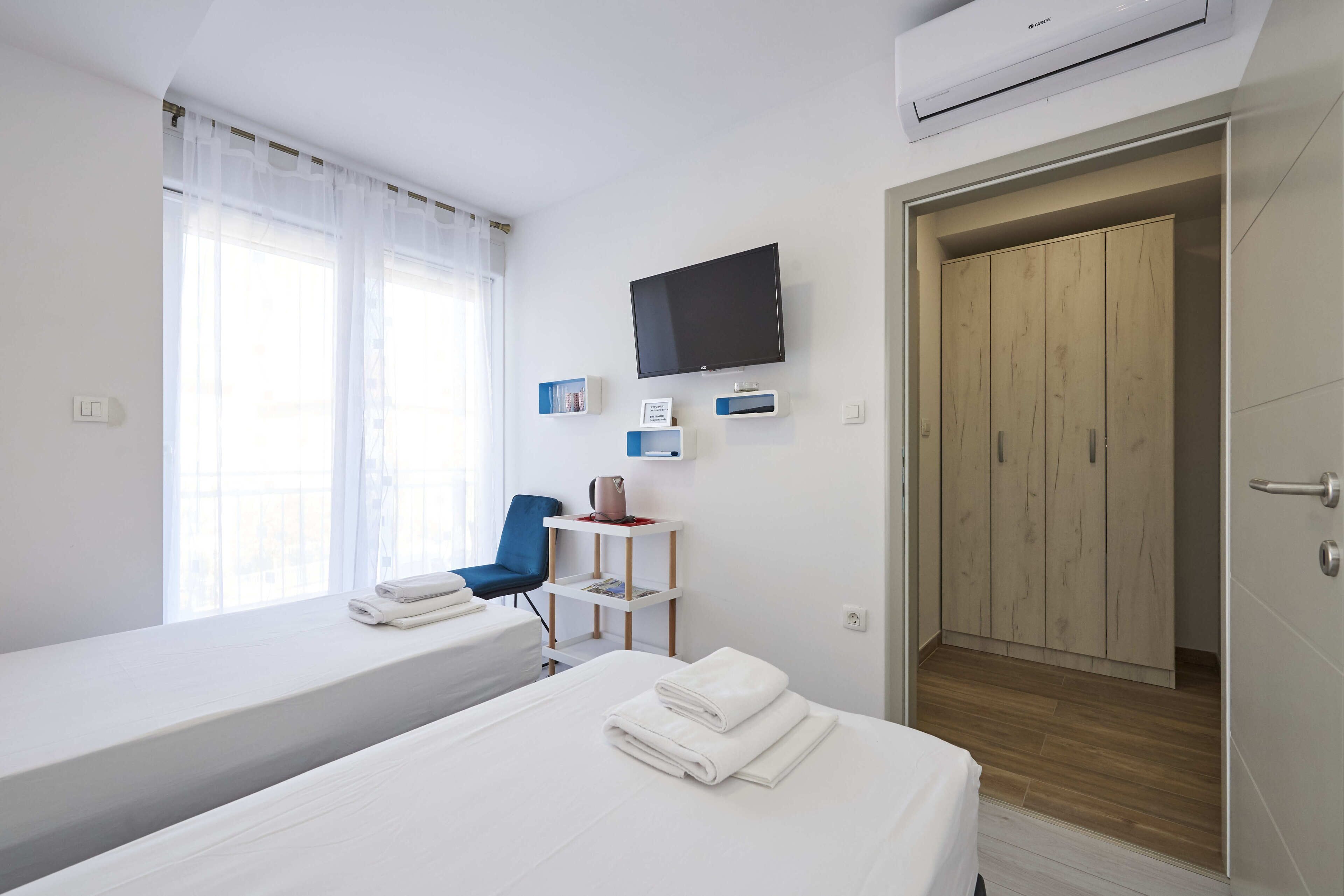 A hotel room with two beds, a TV, a desk with a chair, and a wardrobe.