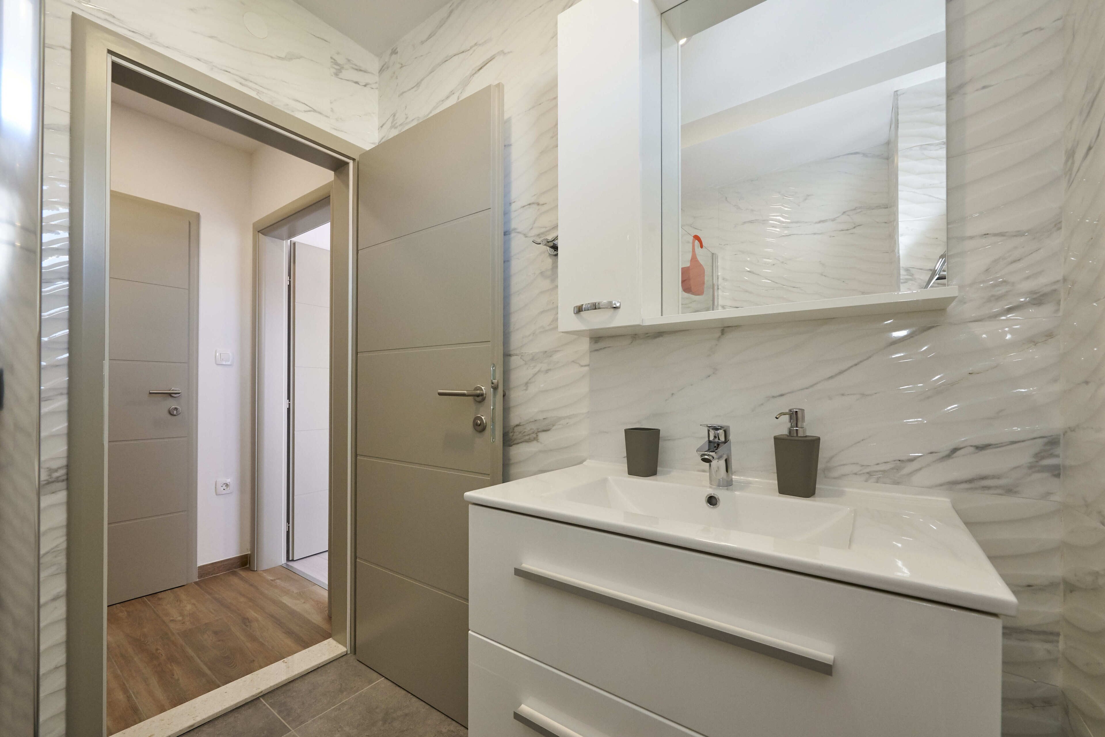 A bathroom with a white vanity, a mirror, and a shower area.