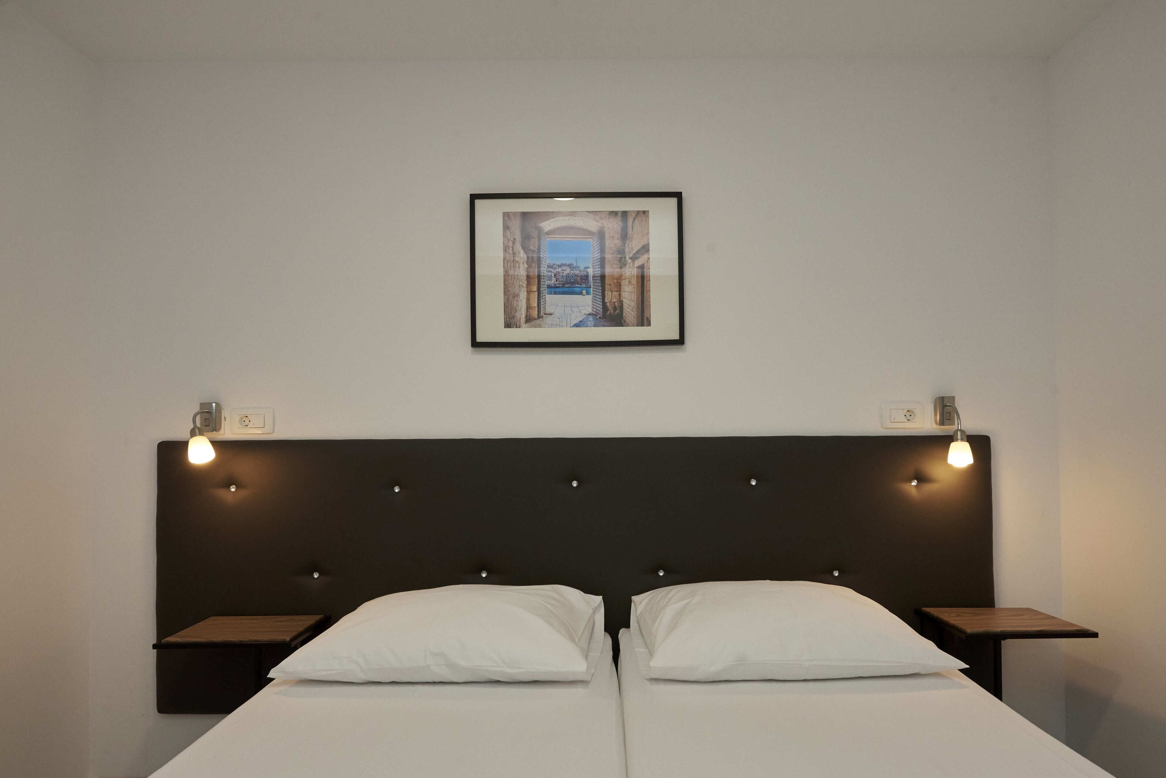 A double bed with a dark headboard and two bedside tables, each with a light fixture. A framed picture hangs above the bed.