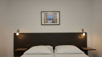 A double bed with a dark headboard and two bedside tables, each with a light fixture. A framed picture hangs above the bed.