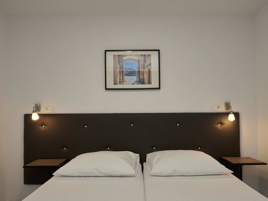 A double bed with a dark headboard and two bedside tables, each with a light fixture. A framed picture hangs above the bed.