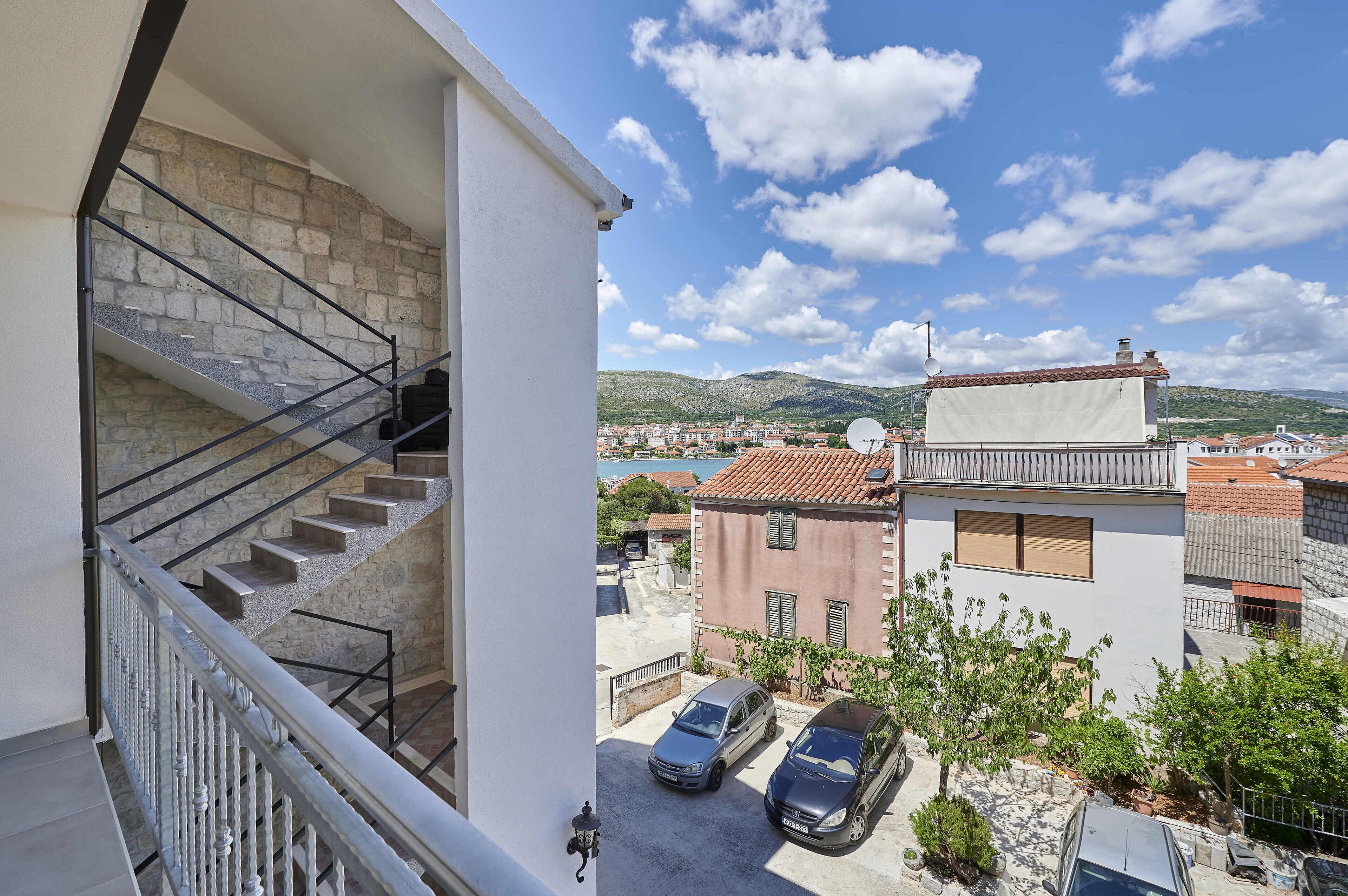 A residential building with a stone staircase, a balcony, and a view of a town and mountains.