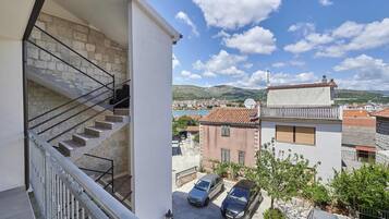 A residential building with a stone staircase, a balcony, and a view of a town and mountains.