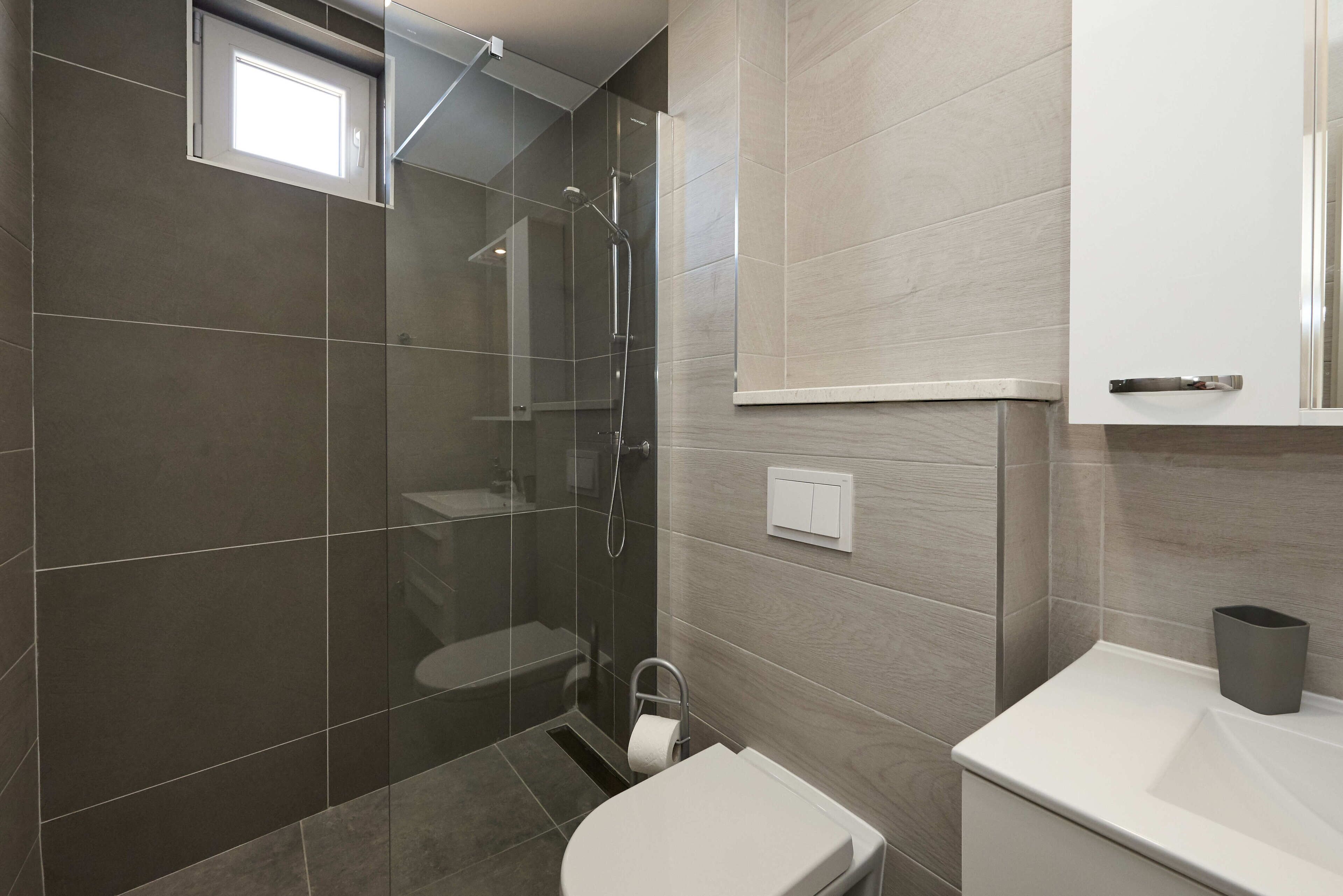 A modern bathroom with a glass-enclosed shower, a toilet, and a sink.