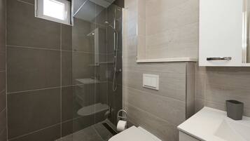 A modern bathroom with a glass-enclosed shower, a toilet, and a sink.