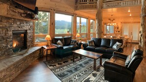 Ein gemütliches Blockhaus-Interieur mit Kamin aus Naturstein, Ledersofas und großen Fenstern mit Blick auf die Berge.