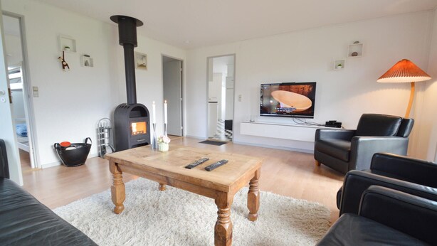 Ein Wohnzimmer mit einem Holztisch, einem schwarzen Ledersofa, einem schwarzen Kamin, einem Fernseher und einer Lampe.