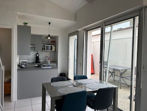 Une cuisine compacte équipée d’un four à micro-ondes et d’un évier, un coin repas avec une table et des chaises, et une porte-fenêtre coulissante donnant sur une terrasse extérieure.