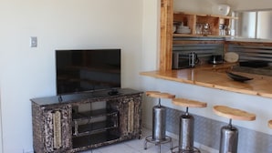 Ett modernt kök med en bänkskiva i trä, barstolar och en tv placerad på ett träskåp.
