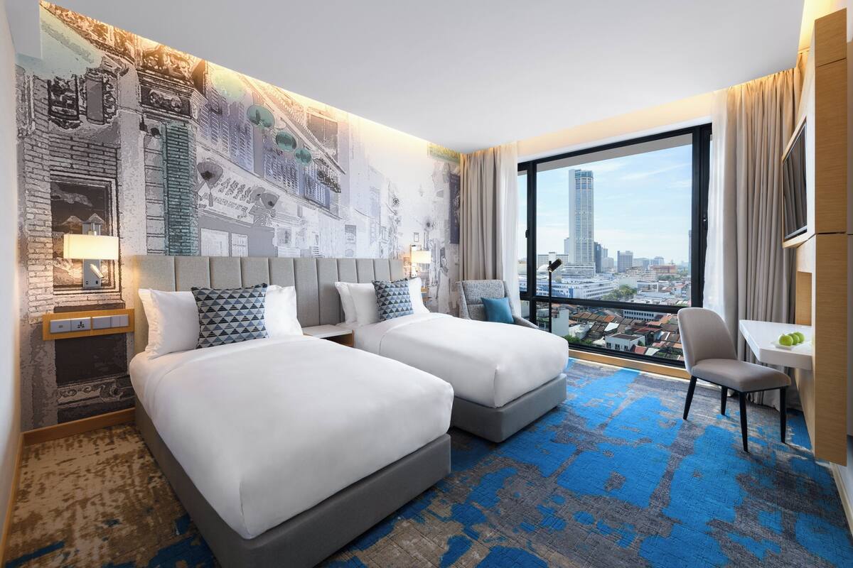 A hotel room with two beds, a city view, a small table, and a chair.
