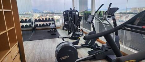 Un gimnasio con máquinas de cardio, equipo de levantamiento de pesas y mancuernas.