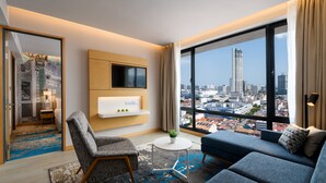 A modern hotel room with a large window, a sofa, a chair, a small table, and a TV mounted on the wall. - OZO George Town Penang (George Town)
