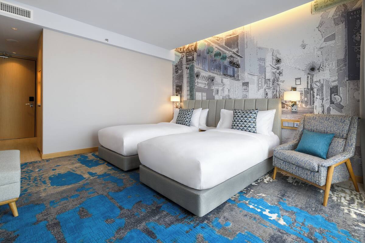 A hotel room with a large bed, two bedside tables, a chair, and a patterned carpet.
