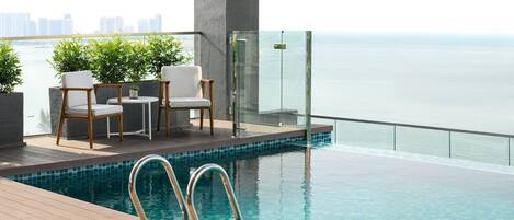 Piscina infinita en la azotea con terraza de madera y dos sillas blancas con cojines.