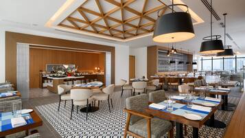 A modern dining area with tables set for service, a kitchen in the background, and a patterned floor.