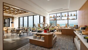 A modern hotel dining area with a buffet setup, large windows, and a view of the sea. - OZO George Town Penang (George Town)