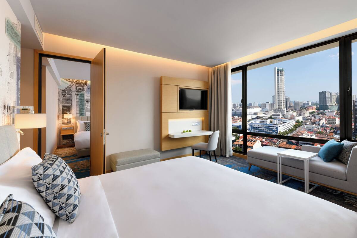 A hotel room with a large bed, a TV, a desk, and a sofa. The room has a city view.