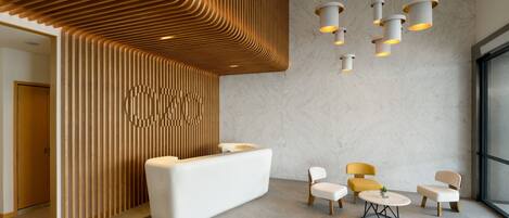 A modern reception area with a white reception desk, wooden slatted wall, and multiple seating options including a round table and chairs.