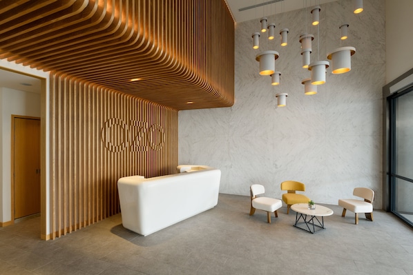 A modern reception area with a white reception desk, wooden slatted wall, and multiple seating options including a round table and chairs.