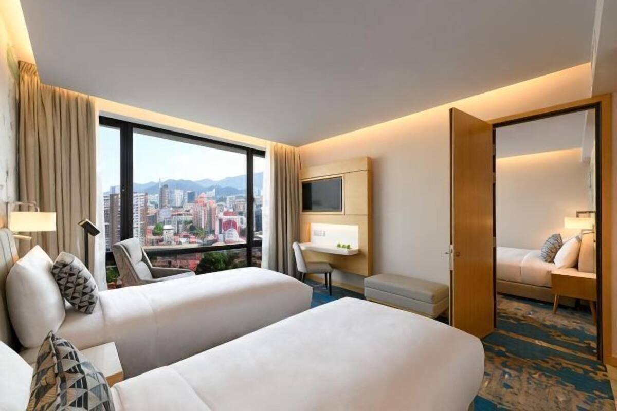 A hotel room with two beds, a desk, a chair, a TV, and a city view.