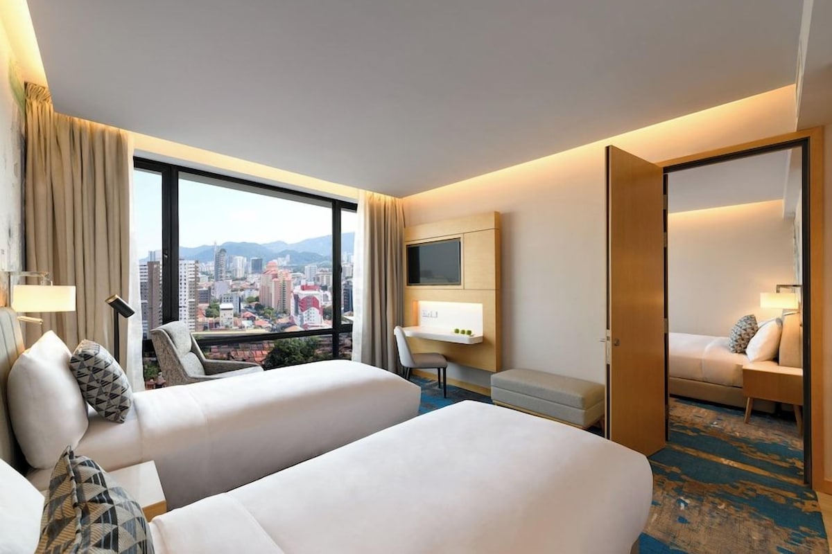 A hotel room with two beds, a desk, a chair, a TV, and a city view.