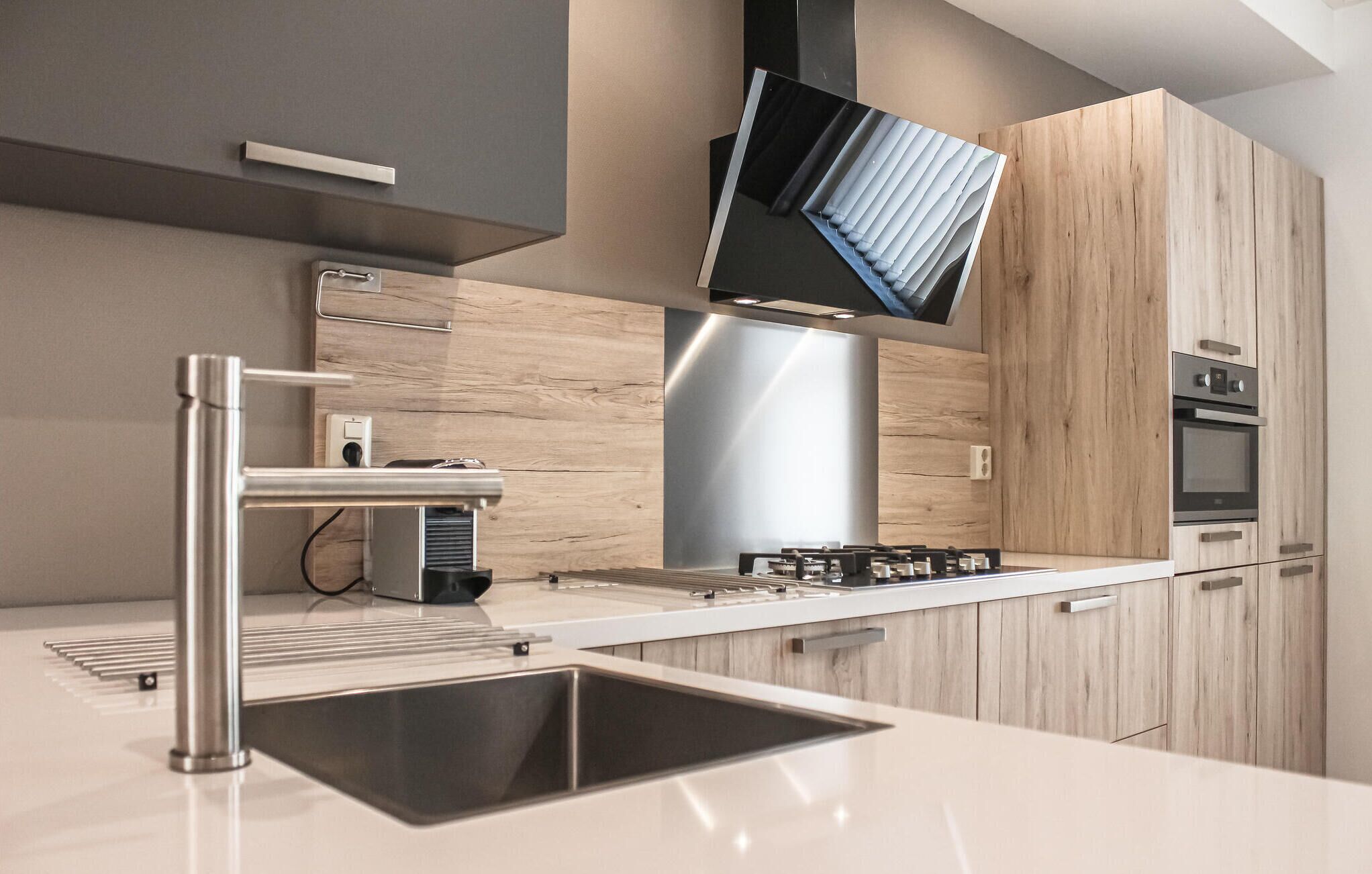 Een moderne keuken met een roestvrijstalen spoelbak, een inbouwoven en een flatscreen televisie die boven het fornuis is bevestigd.