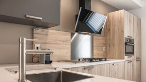 Een moderne keuken met een roestvrijstalen spoelbak, een inbouwoven en een flatscreen televisie die boven het fornuis is bevestigd.