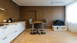 Una cocina moderna con armarios blancos, una mesa de comedor de madera y un televisor sobre un mueble.