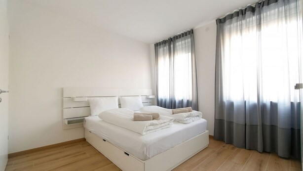 Un dormitorio moderno con una cama blanca, cabecera y ventana con cortinas.